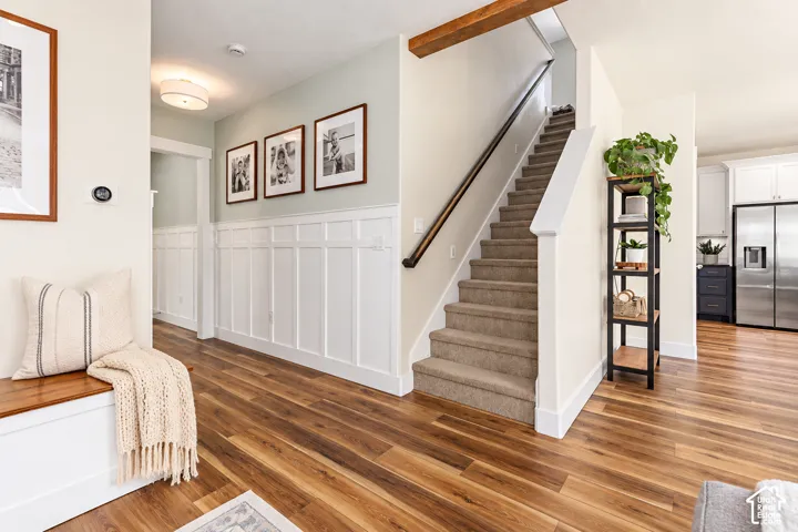 Wainscoting detailing, staircase with carpeted treads, exposed wood beam, and stainless steel appliances