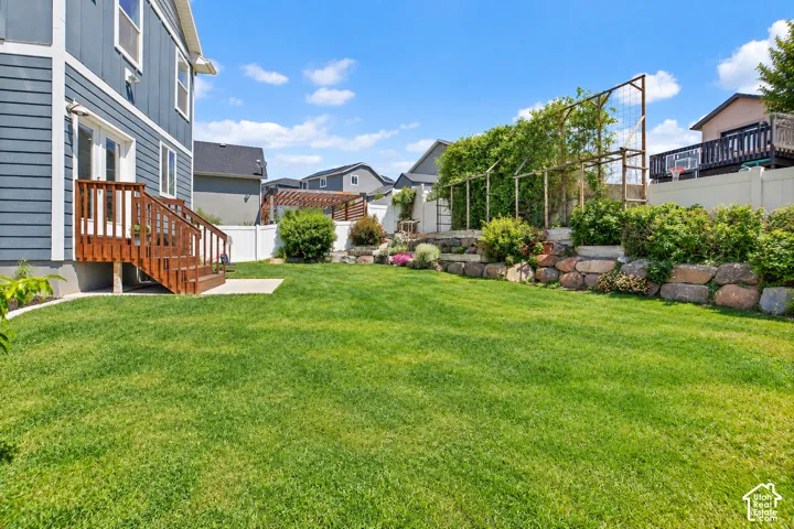 Expansive lawn with a two-tier stone retaining wall, mature landscaping, and a white privacy fence