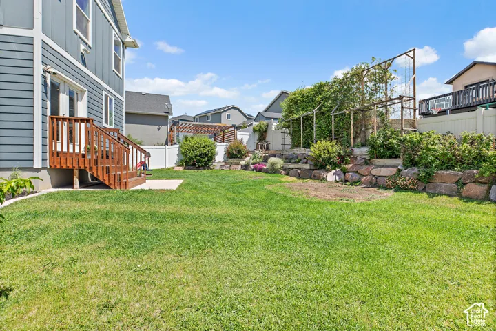 Expansive backyard featuring a manicured lawn, multi-level landscaping with rock retaining walls, and a wooden deck with stairs