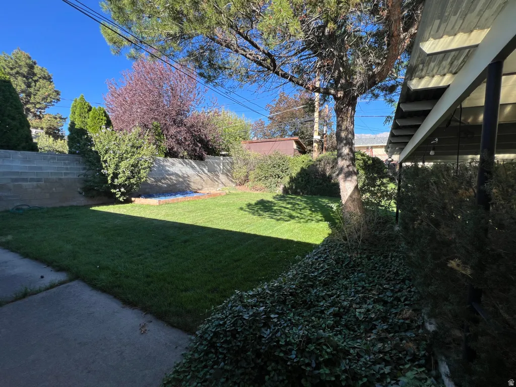 Choice backyard featuring a manicured lawn, concrete patio, and a block retaining wall with mature trees and established greenery