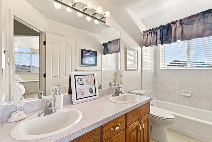 Dual vanity with wood-finish cabinetry, built-in mirror, and overhead lighting