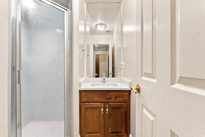 Shower enclosure with textured glass, wood-finish vanity with countertop, and integrated sink