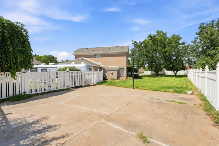Expansive concrete driveway, white privacy fencing, and a manicured lawn area