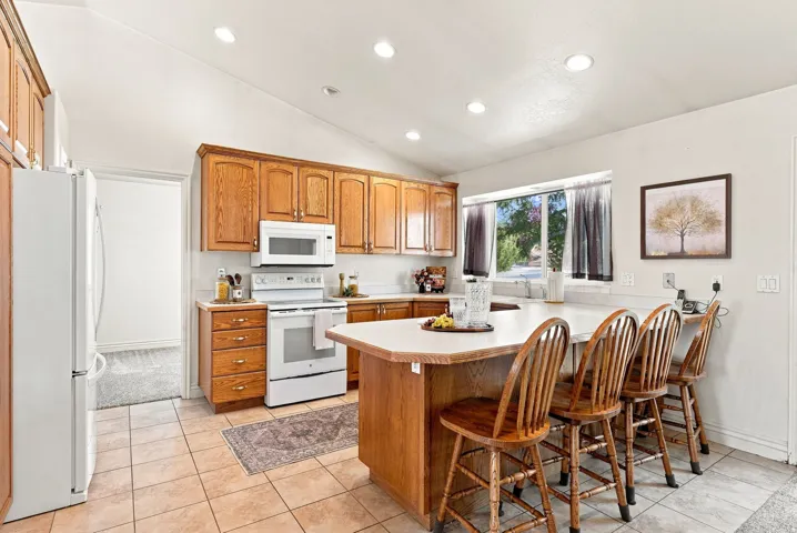 Kitchen featuring wood cabinetry, white appliances, a center island with seating, recessed lighting, and tile flooring