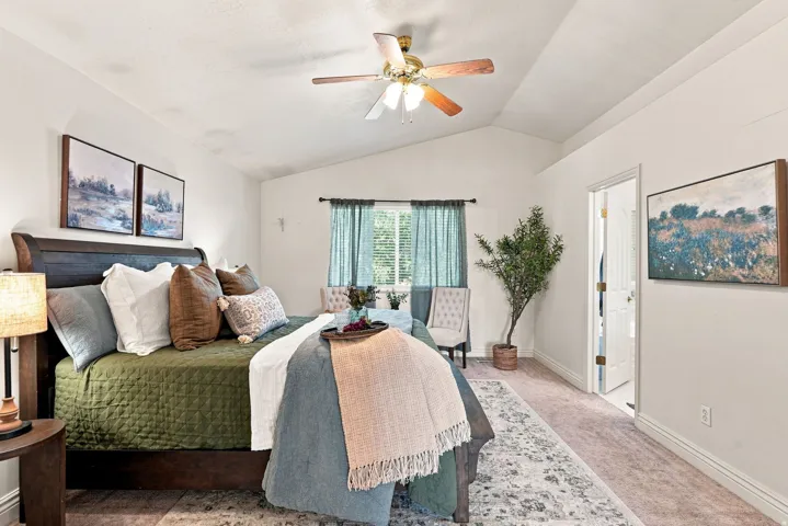 Primary bedroom suite featuring a vaulted ceiling with ceiling fan, wood-finish flooring, and expansive windows with light filtering curtains
