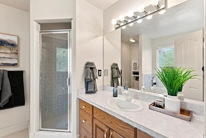 Shower enclosure with tile surround, vanity with wood cabinetry, integrated sink, and large wall-mounted mirror