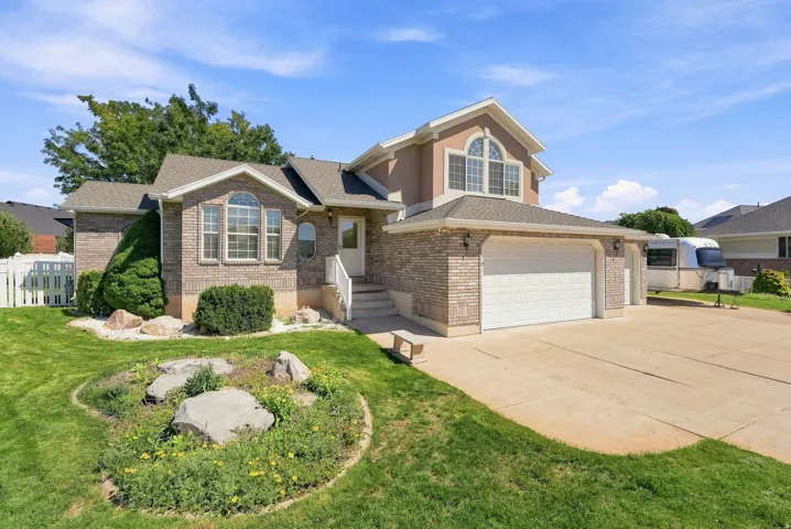 Brick and stucco exterior, arched windows, attached garage, concrete driveway, and a white picket fence