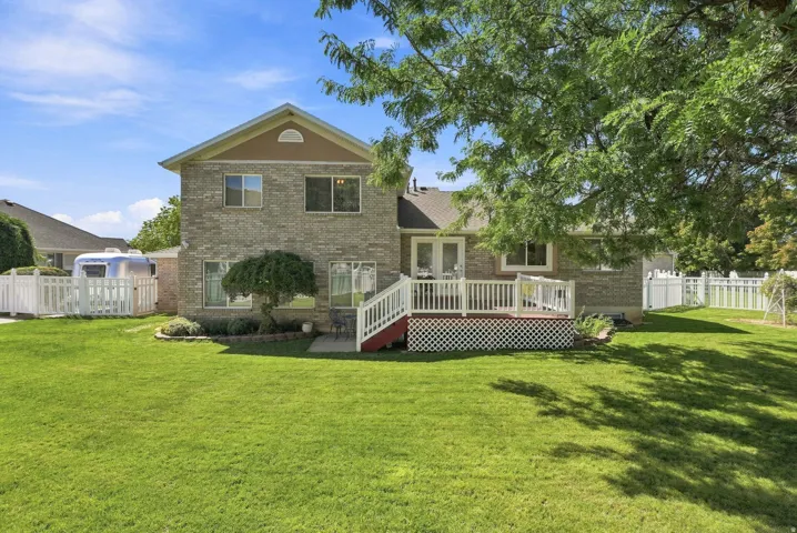 Expansive green lawn with mature trees, brick exterior, white picket fencing, and a multi-level deck with white railings