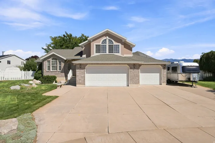 Two-story property featuring a brick and stucco exterior, arched window details, a three-car garage, and an expansive concrete driveway