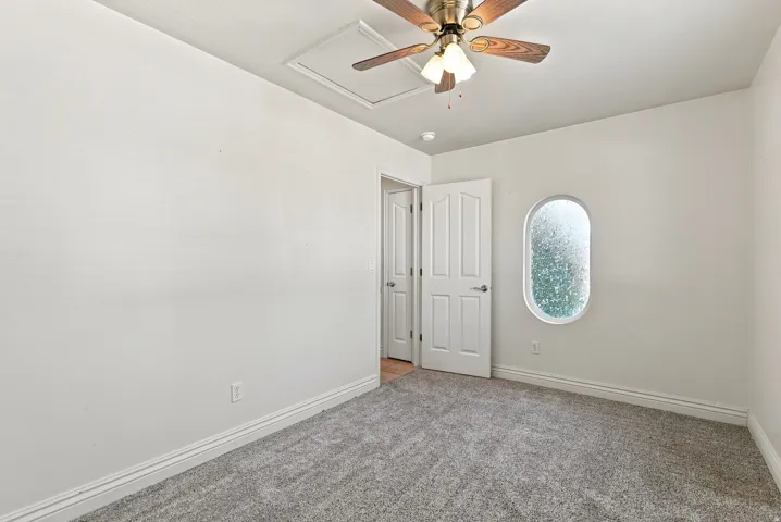 Plush carpet flooring, white painted walls, a ceiling fan with light fixture, and a unique oval window