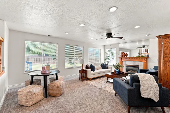 Recessed ceiling lighting, ceiling fan, multiple windows with blinds, built-in fireplace with wood mantel and tile surround, and wood-finish flooring
