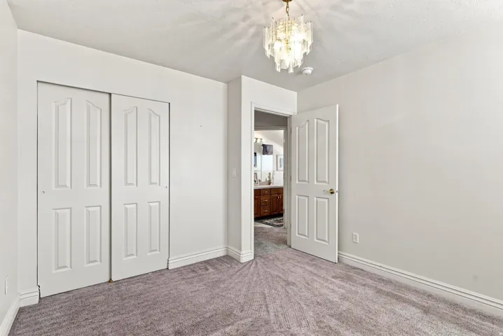 Textured carpet flooring, panelled bi-fold closet doors, elegant ceiling-mounted light fixture, white interior door with brass hardware, and white wall finishes