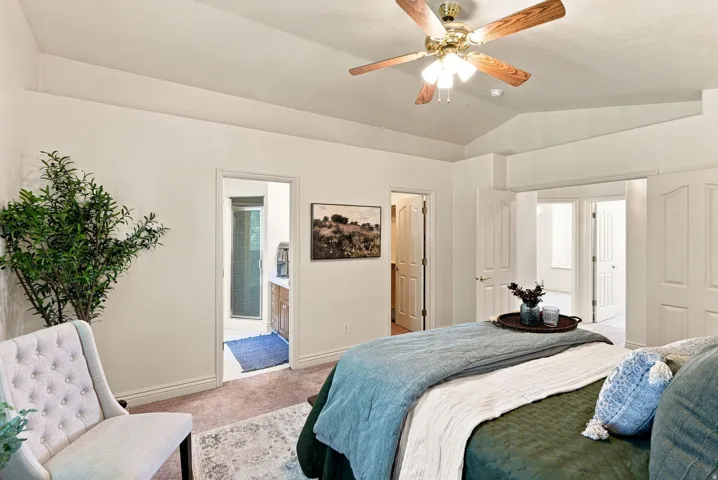 Vaulted ceiling with a wood-finish ceiling fan, carpeted flooring, and white interior doors