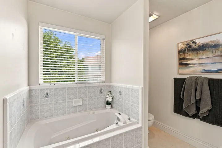 Built-in jetted tub, tiled surround, and natural light from the window