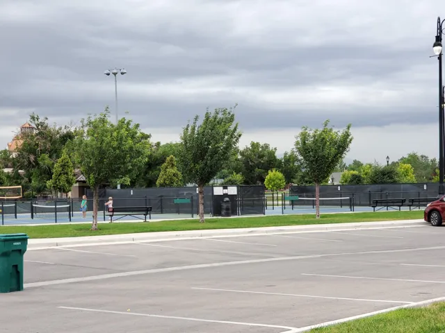 Tennis courts with perimeter fencing, a volleyball net, and surrounding trees