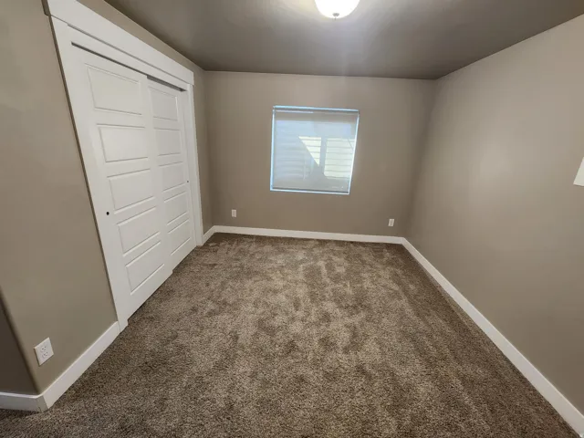 Carpeted room with a window featuring blinds, an overhead flush-mount light fixture, and a closet with white paneled bi-fold doors