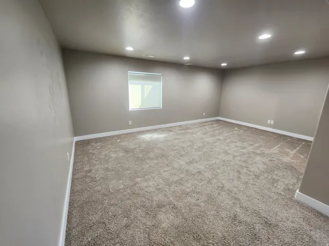 Recessed ceiling lighting, neutral wall paint, white trim, window with roller shade, and plush carpet flooring