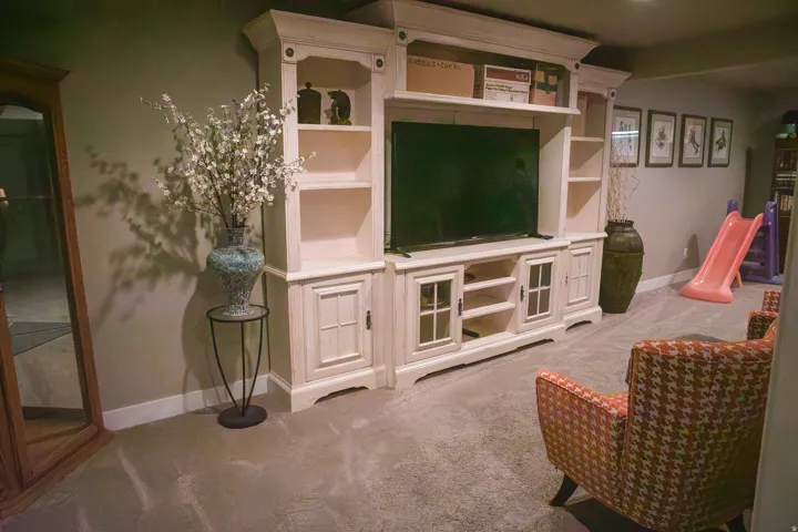 Wall-mounted media console with built-in shelving, glass-front cabinetry, and textured carpeting