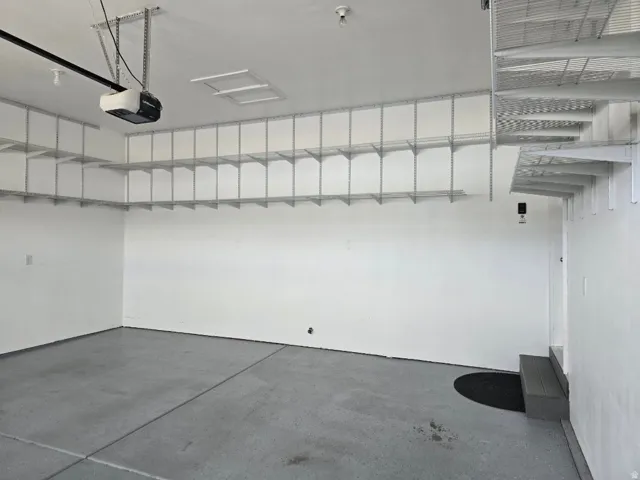 Garage featuring an overhead door opener, overhead lighting, integrated wall shelving, a built-in step, and a concrete floor