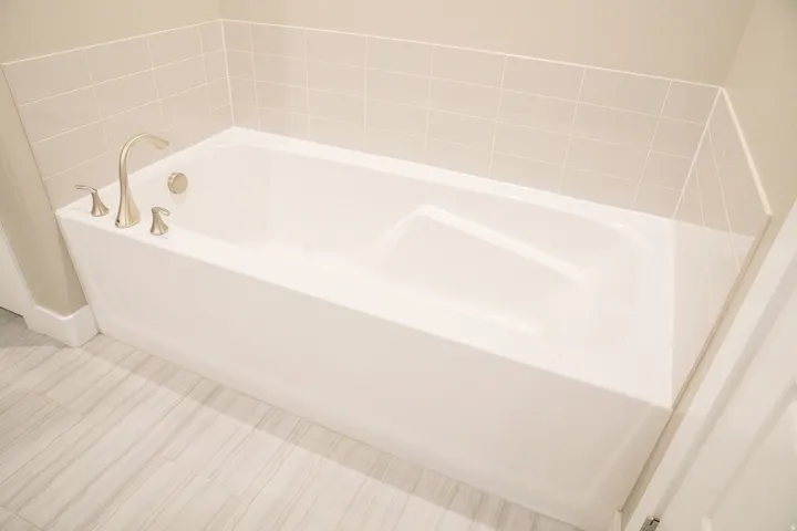 Alcove bathtub featuring a brushed nickel faucet and tile surround, complemented by wood-finish flooring