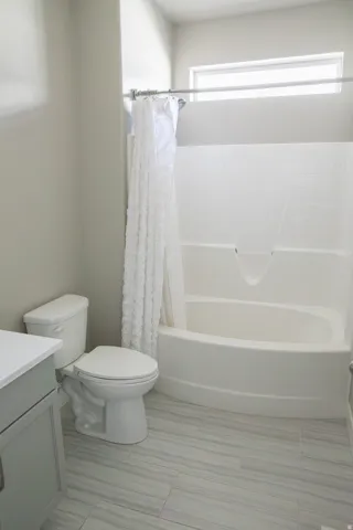 Ceramic tile flooring, white bathtub and shower combination, white toilet, light gray vanity with white countertop, and high transom window