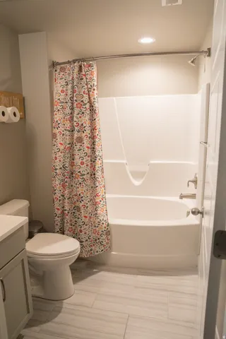 Built-in bathtub with shower, toilet, single vanity with light-toned cabinetry, light-toned countertop, and tile flooring