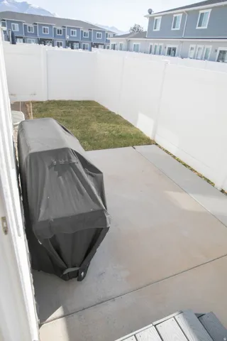 Rear yard featuring a concrete patio, white vinyl fencing, and a patch of natural grass