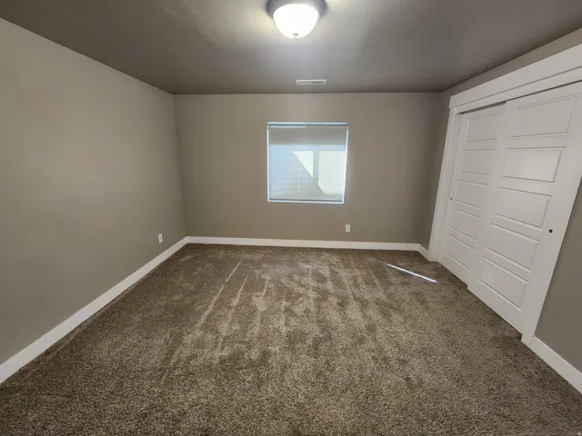 Textured carpet flooring, window with roller shade, white trim, and a built-in closet with panel doors