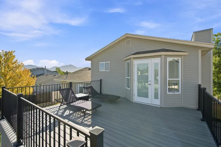 Spacious outdoor deck with a gray composite surface, black metal railings, and a bay window with double French doors