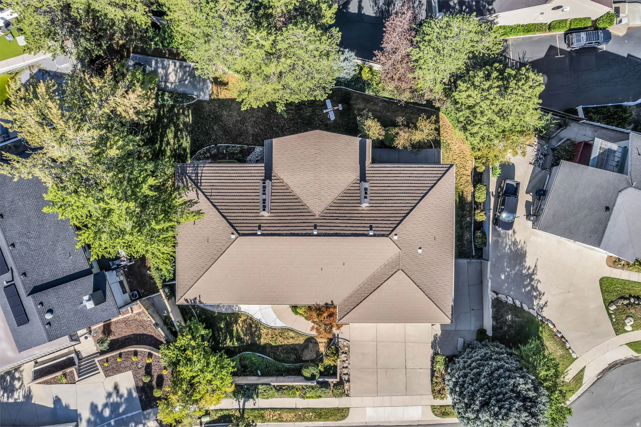 Gable roof with integrated chimneys, mature perimeter trees, concrete driveway, and landscaped front yard