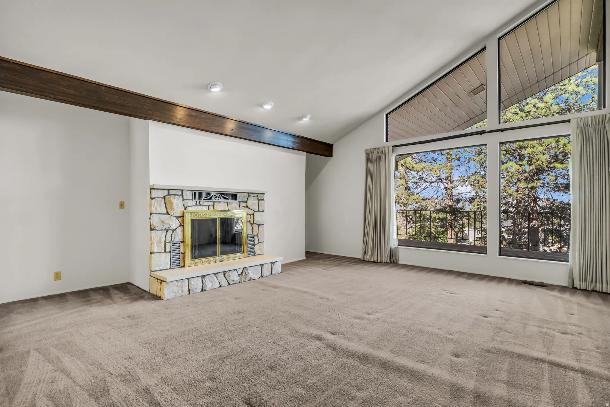 Vaulted ceiling, exposed wood beam, stone-surround fireplace with hearth, and extensive window system