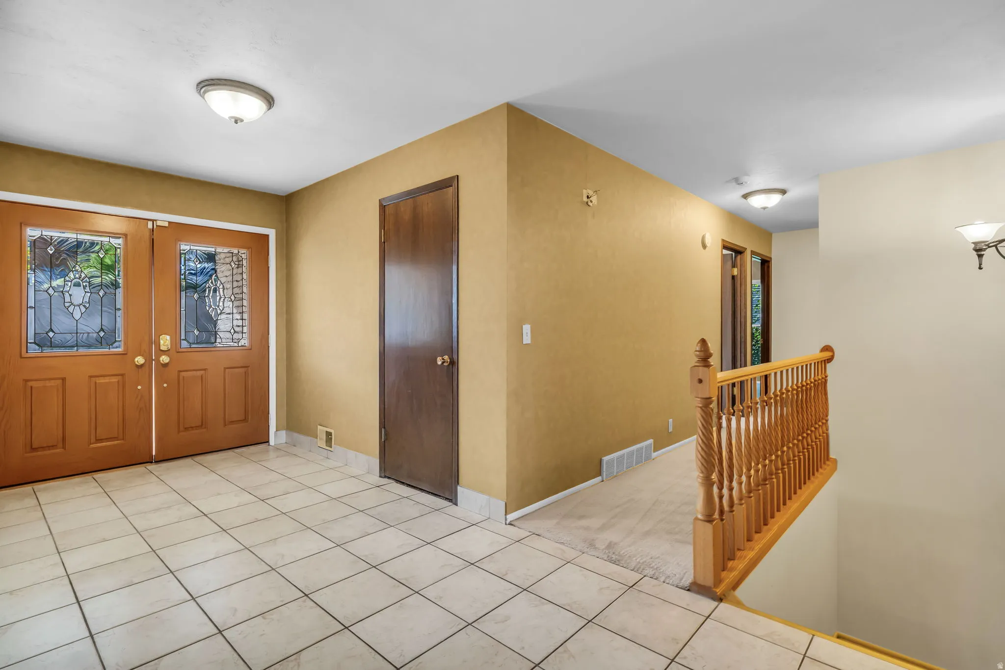 Double entry doors with leaded glass inserts, tiled flooring, wood railing, and flush-mount lighting fixtures