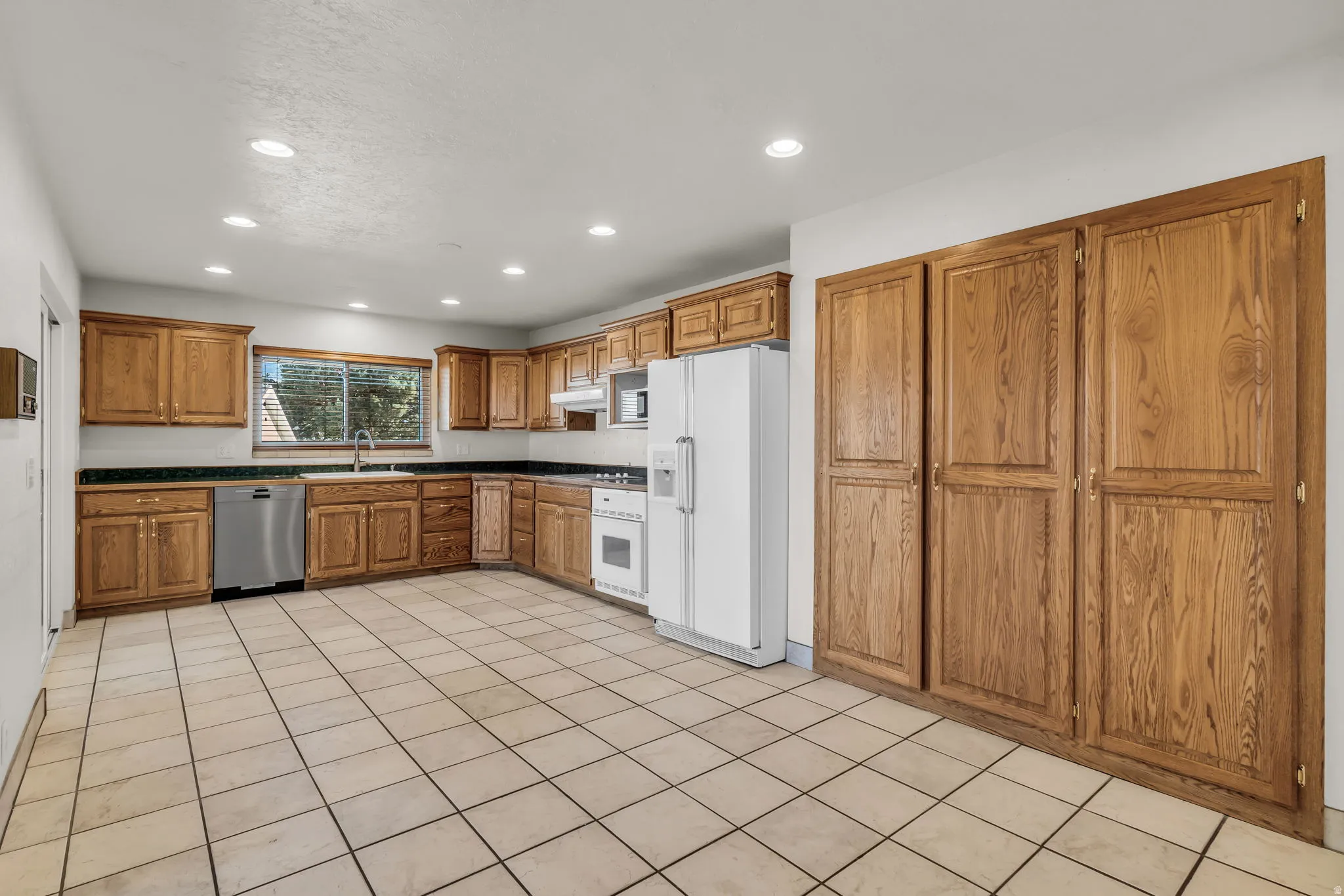 Expansive kitchen featuring wood cabinetry, tile flooring, recessed lighting, and a stainless steel dishwasher