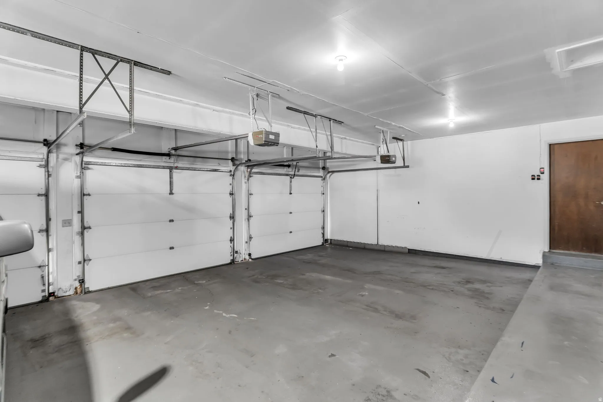 Two white garage doors with automatic openers, concrete flooring, and a single wood-finish door