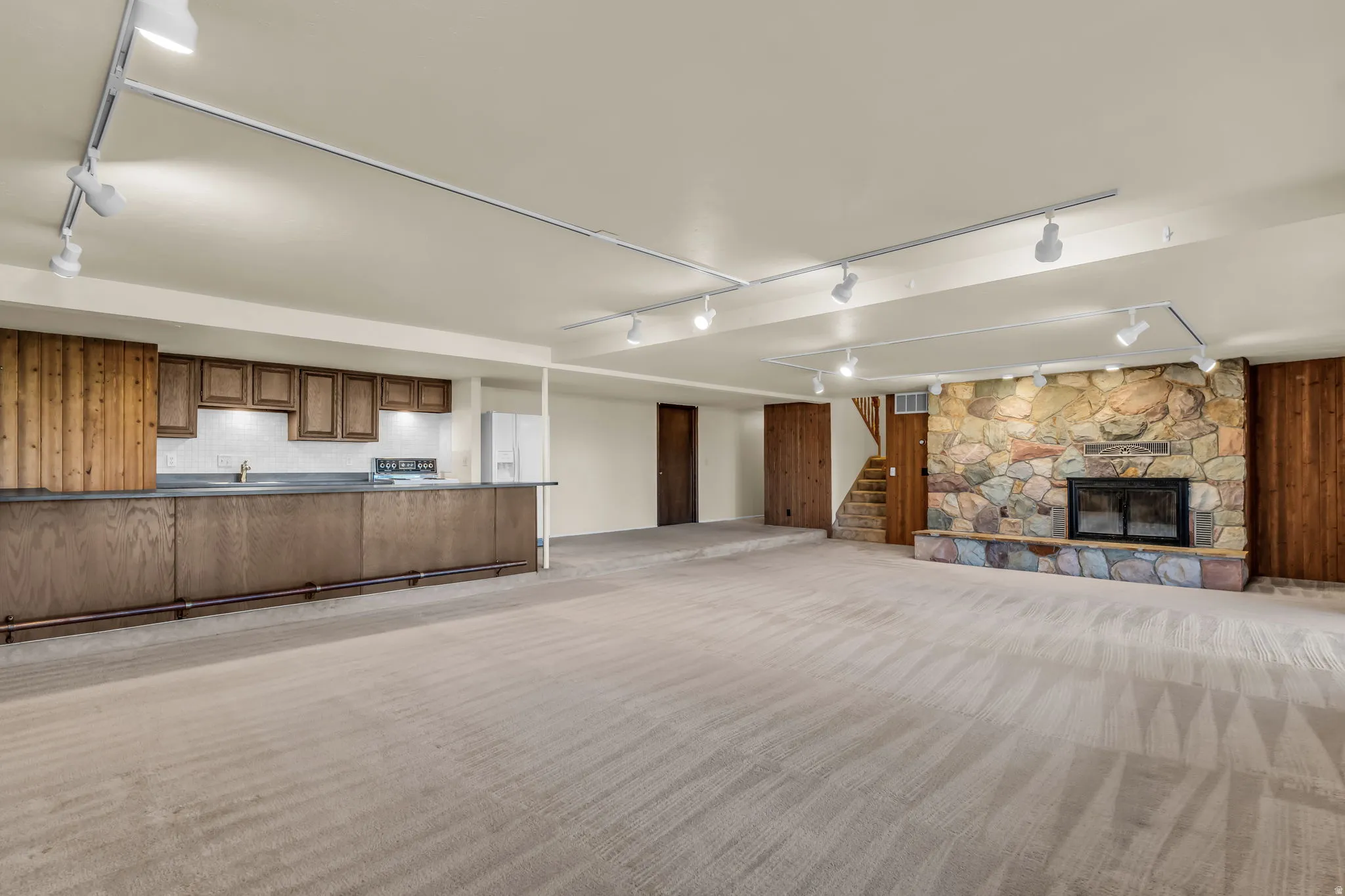 Spacious open-concept lower level featuring a stone-clad fireplace and a built-in wet bar with wood-finish cabinetry