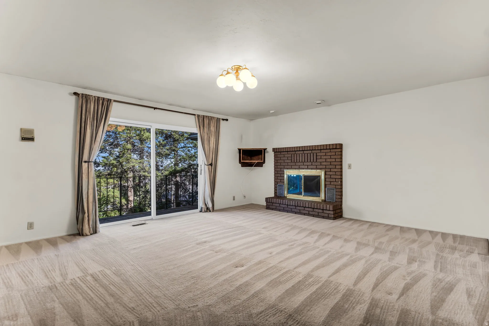 Spacious primary suite featuring a brick fireplace, a ceiling-mounted light fixture, and glass sliding doors leading to an outdoor balcony with metal railings
