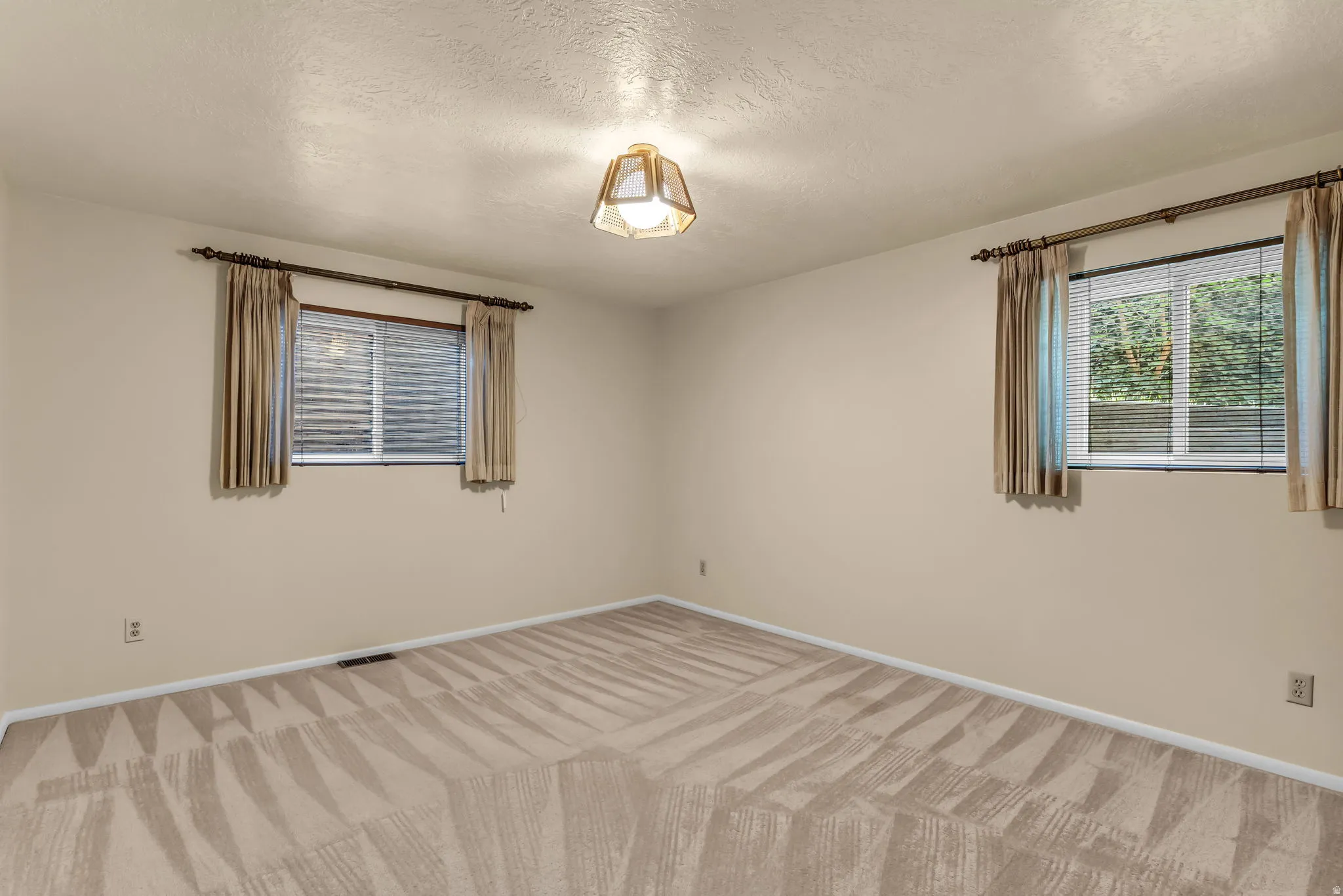 Neutral tone wall paint, patterned carpeting, and a central ceiling light fixture