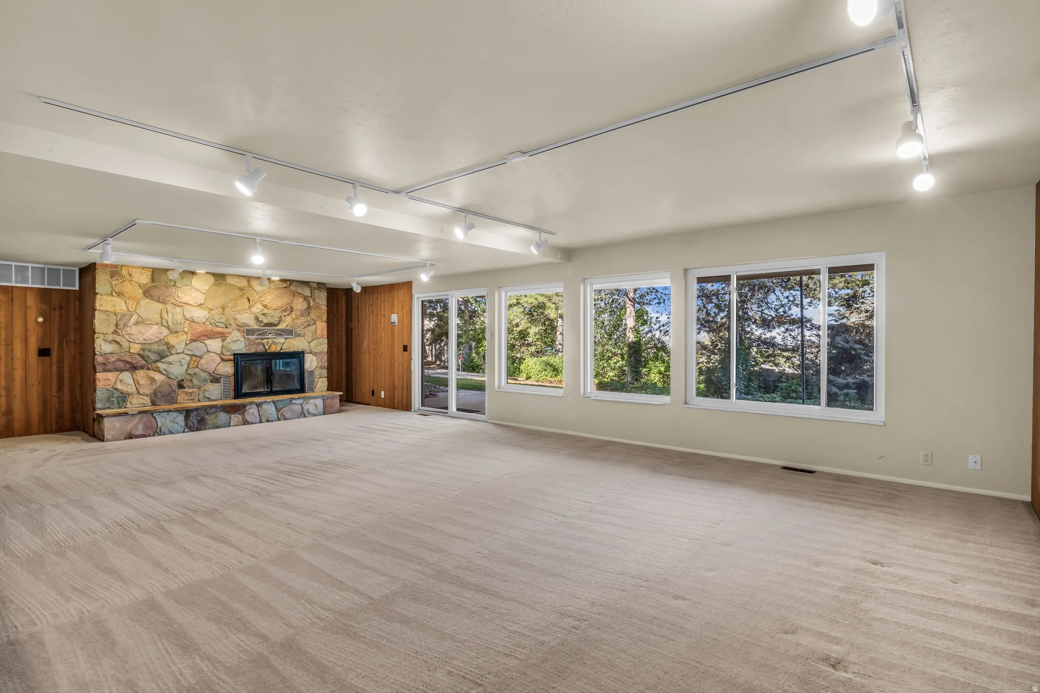 Spacious room featuring a stone-clad fireplace, built-in fireplace insert, track lighting, and multiple windows