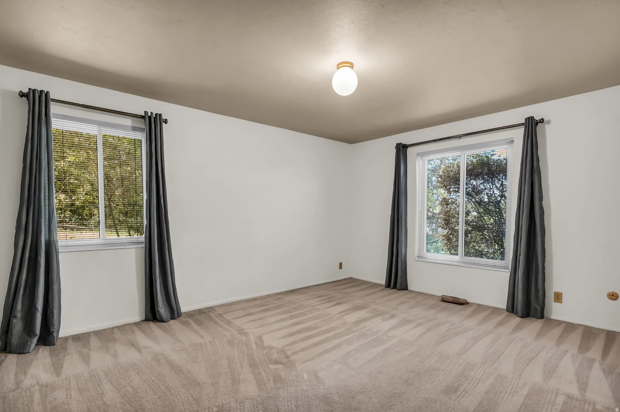 Neutral wall paint, two large windows, overhead flush-mount lighting, and patterned carpeting
