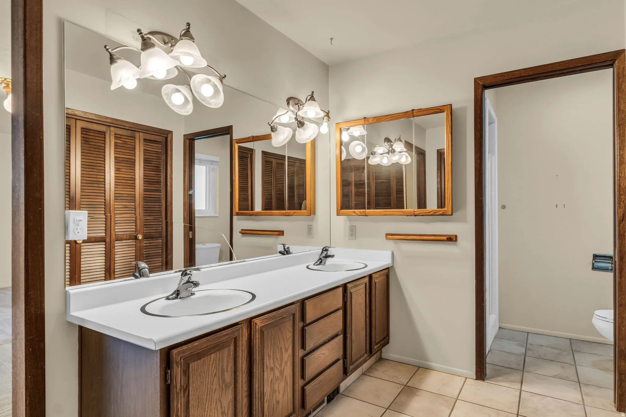 Primary ensuite featuring double vanity with integrated sinks, wood-finish cabinetry, chrome faucets, and tile flooring