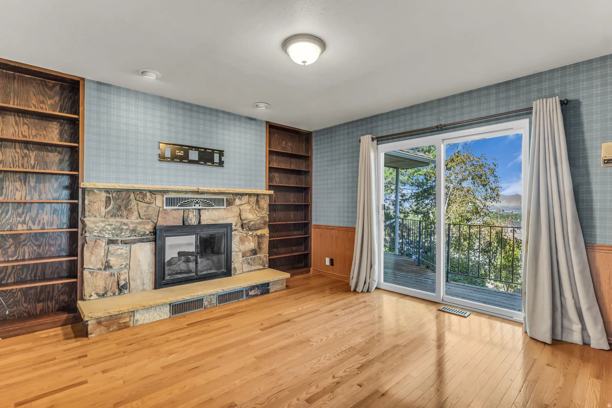 Hardwood flooring, a stone-clad fireplace, integrated shelving, and a sliding glass door to an outdoor deck