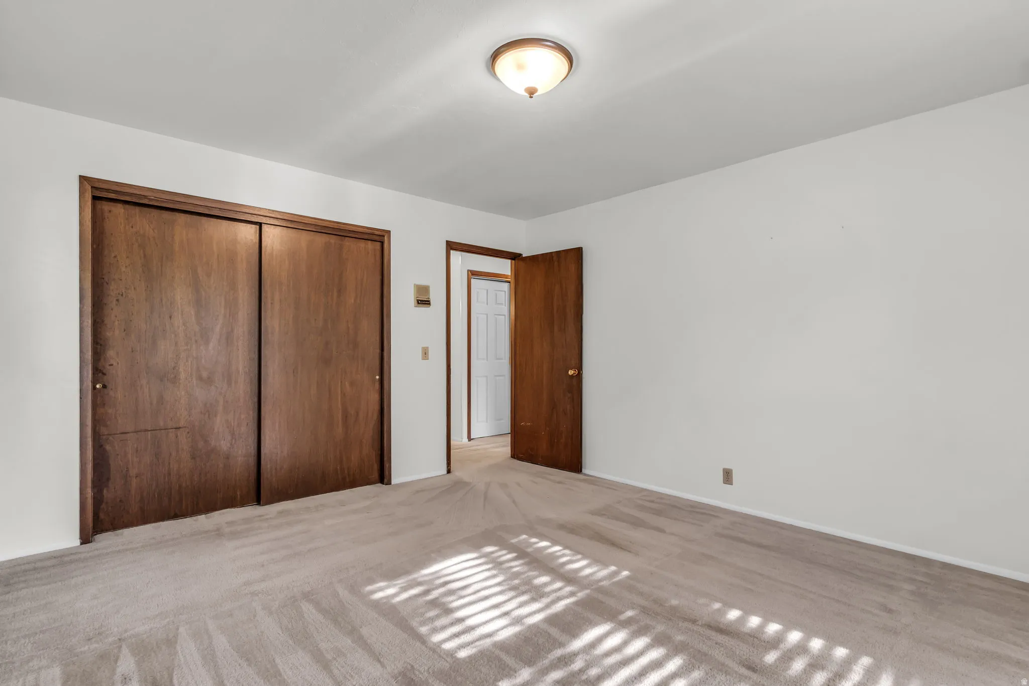 Light-colored wall-to-wall carpeting, white walls, wood-finish bi-fold closet doors, and a flush-mount ceiling light fixture