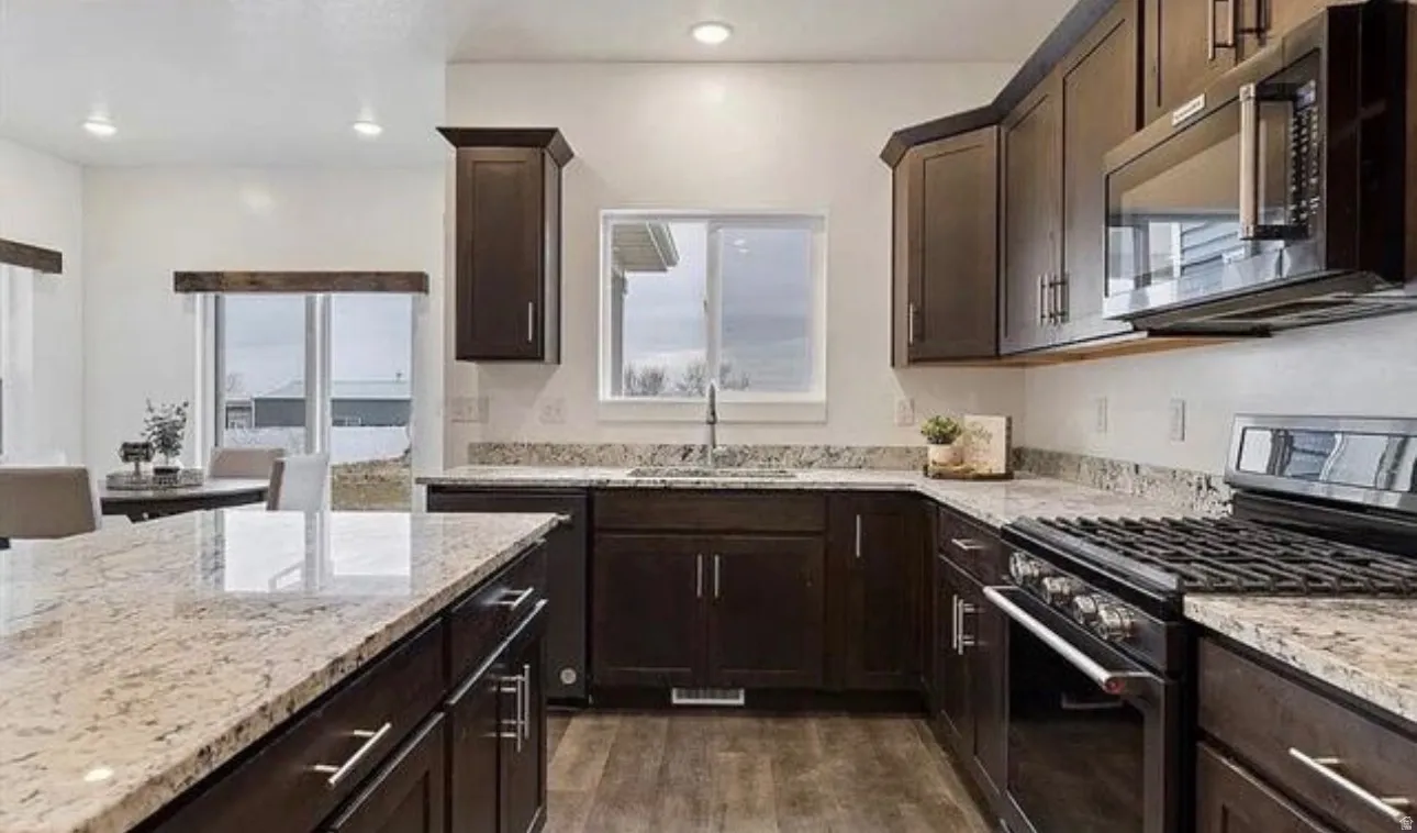 Kitchen featuring dark wood-finish cabinetry, light-toned granite countertops, a built-in microwave, a gas range, and recessed lighting