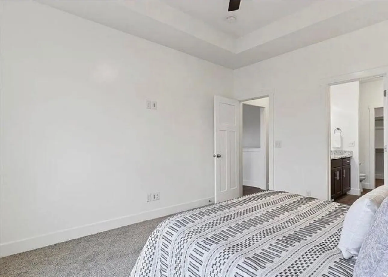Tray ceiling with a ceiling fan, white paneled doors, and gray carpet flooring