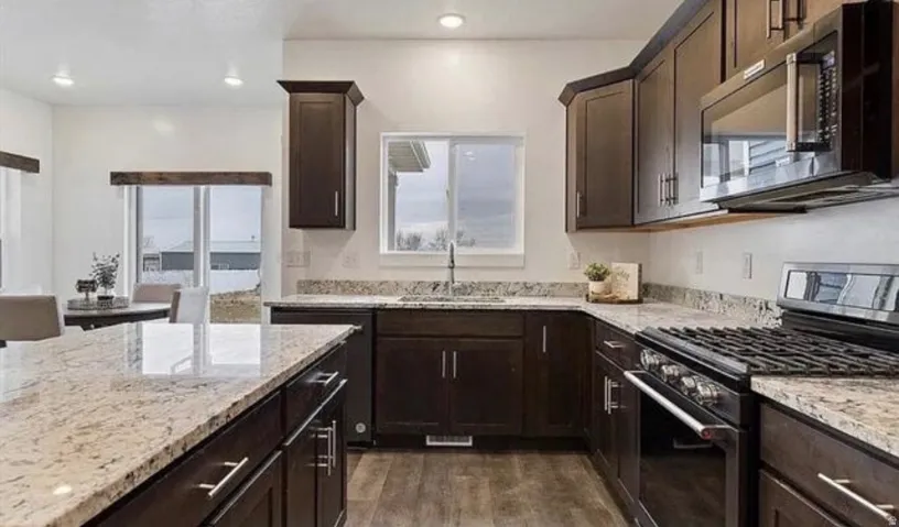 Kitchen featuring dark wood-finish cabinetry, light-toned granite countertops, a built-in microwave, a gas range, and recessed lighting