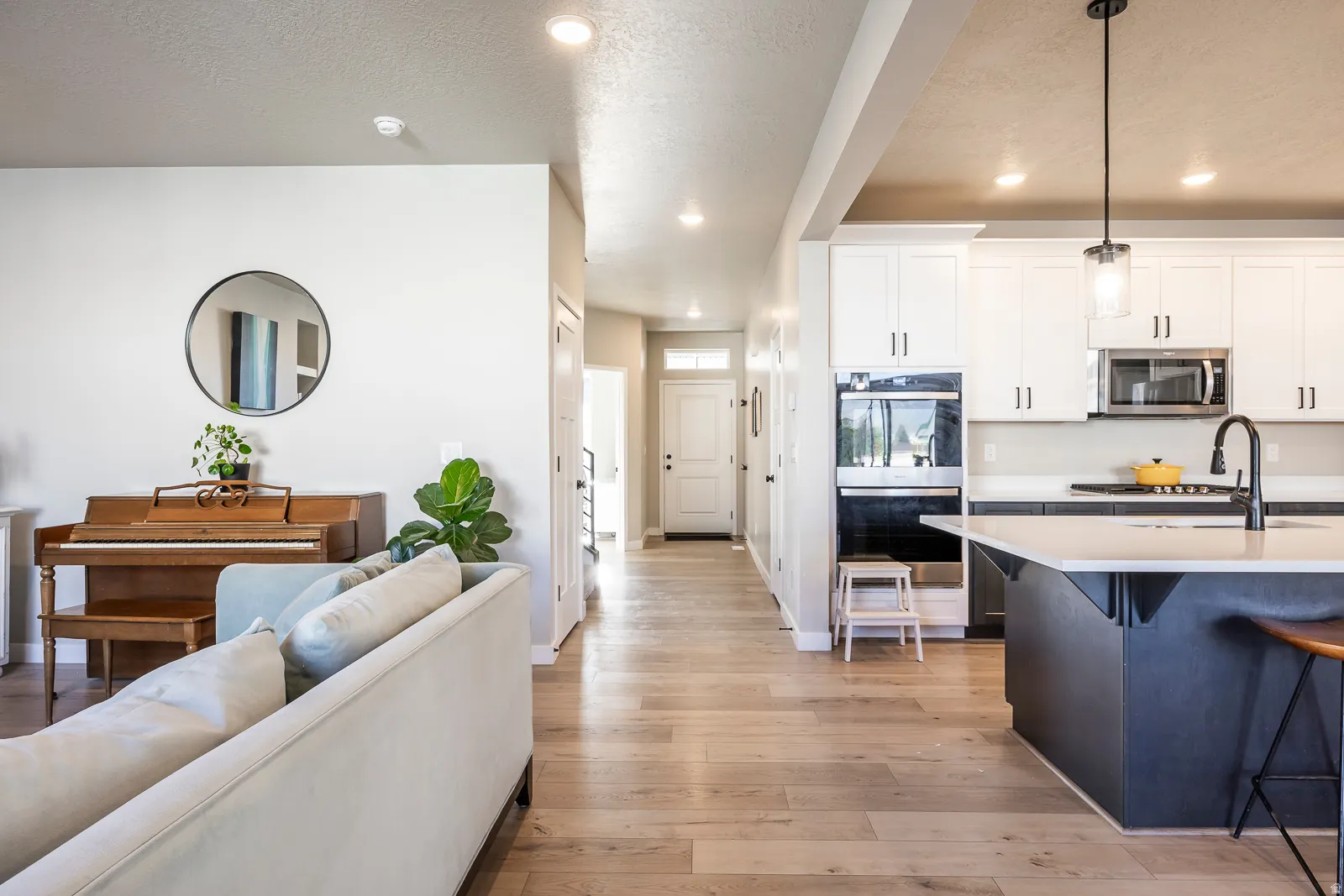 Open-concept living space featuring wood-finish flooring, recessed lighting, and a kitchen with white cabinetry, built-in appliances, and a central island with a pendant light