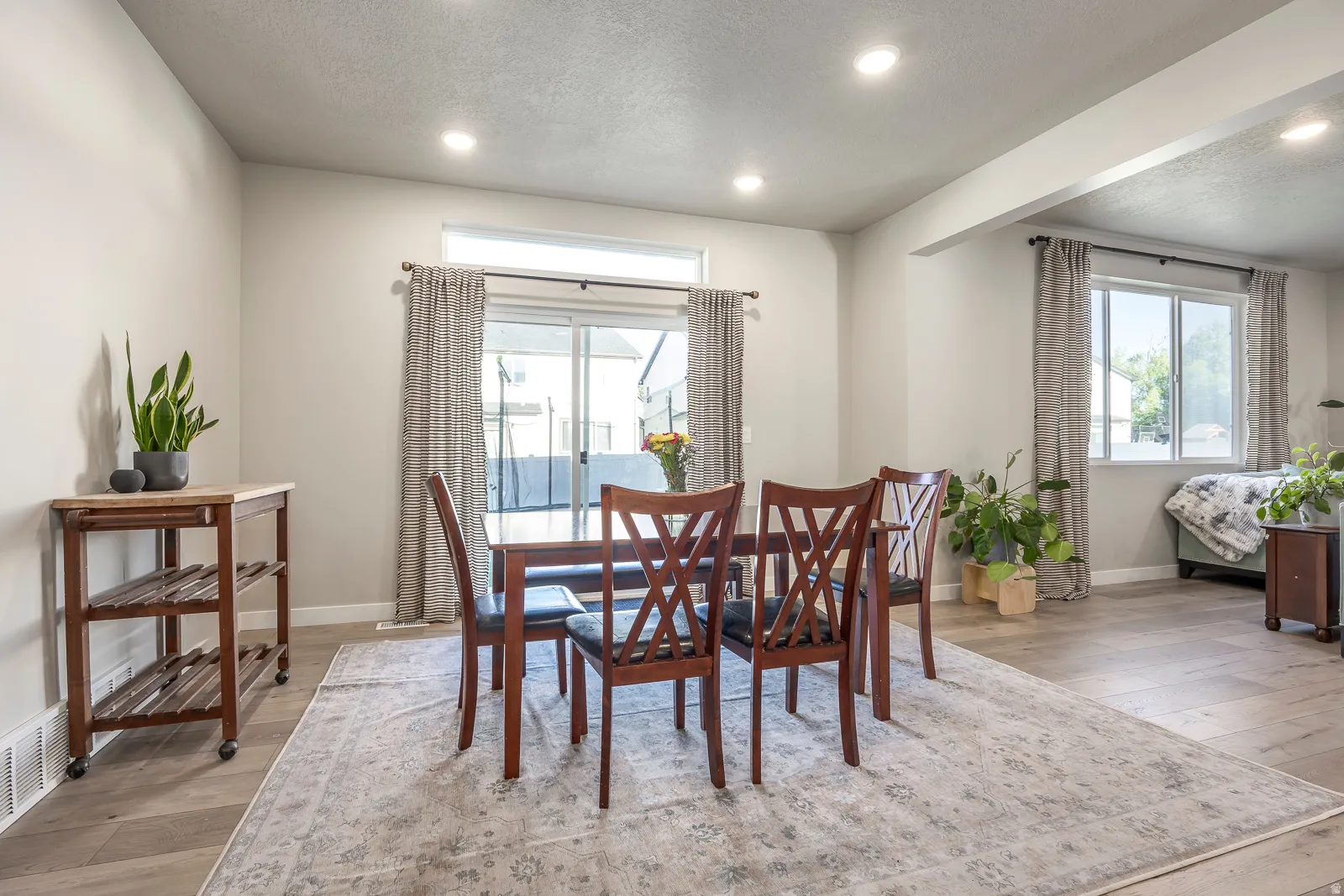 Recessed lighting illuminates the dining area, featuring light wood-finish flooring and a sliding glass door