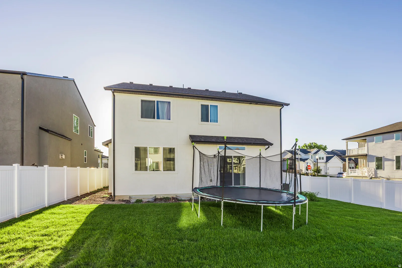 Expansive backyard featuring a manicured lawn, white privacy fencing, and a stucco exterior
