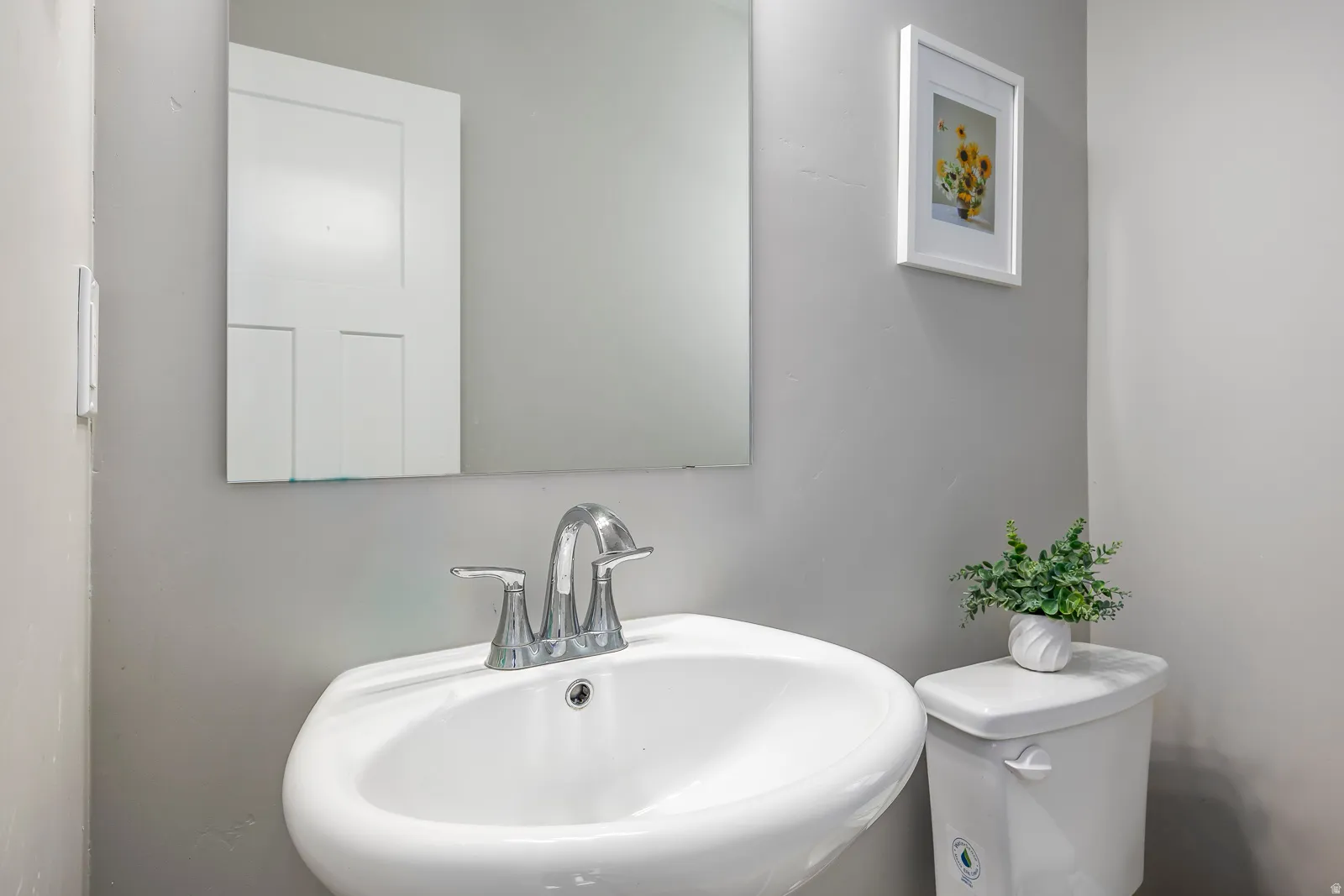 Pedestal sink with chrome fixtures and a wall-mounted mirror