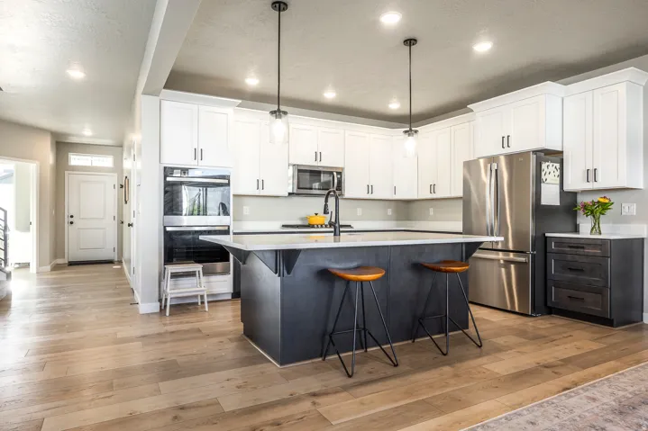 Kitchen featuring a dark-toned island, white shaker-style cabinetry, stainless steel appliances, and light wood-finish flooring